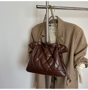 Close-up of brown quilted PU leather bucket bag with gold chain strap on a chic outfit