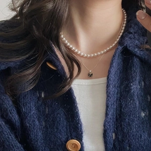 Close-up of double-layer necklace with white pearls and square green gemstone pendant