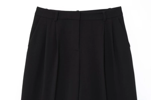 Détail du pantalon noir avec des plis profonds et une texture de tissu sergé haut de gamme