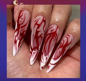 Macro shot of long stiletto press-on nails with red blood splash and flame gradient patterns