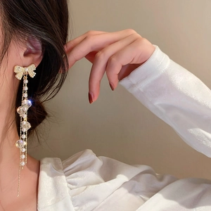 Gros plan détaillé des boucles d'oreilles nœud avec longs pompons dorés et perles
