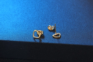 Macro shot of minimalist hollow heart-shaped gold studs with matte navy background