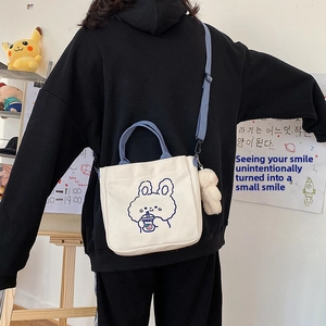 Detail of cute canvas tote bag with blue rabbit print and white plush charm accessory