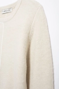 Close-up of beige knit sweater texture with soft plush fabric and collar label detail