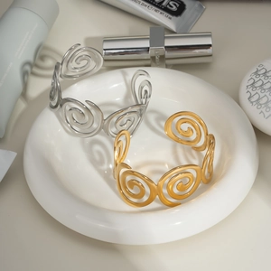 Detail of gold and silver spiral textured open bracelets on a minimalist display