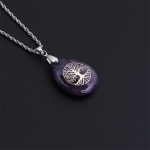 Dettaglio macro del ciondolo a goccia viola con albero della vita dorato su catena argento