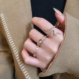 Detailed view of gold snake ring with white stones and pink heart gemstone set on hand