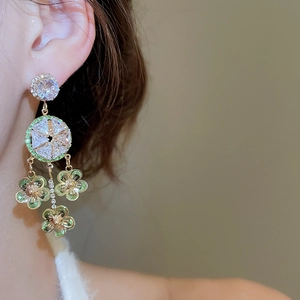 Macro shot of silver needle floral earrings featuring green zircon petals and golden tassels