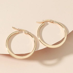 Detailed macro shot of large gold hoop earrings with secure hinge closure on a stone surface