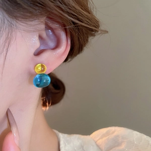 Close-up of yellow and blue spherical resin stud earrings worn on a woman's ear