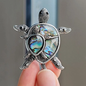 Detail of a turtle brooch featuring iridescent abalone shell and silver metallic texture