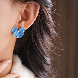 Vue rapprochée d'une boucle d'oreille fleur bleue avec bords dorés sur l'oreille du mannequin