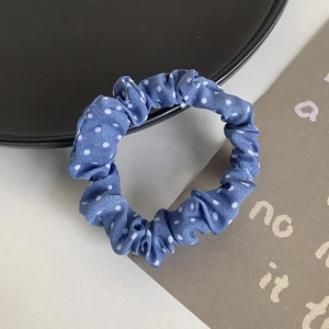 Blue polka dot scrunchie fabric hair tie displayed on a stylish flat lay decorative plate