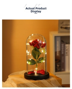Close-up of a red preserved rose in a glass dome with warm LED fairy lights on a wooden base