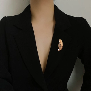 Elegant gold feather brooch with white pearl on a black blazer lapel for women
