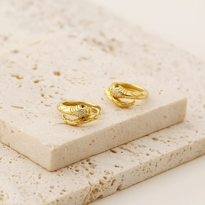 Detailed view of gold snake-shaped ear cuffs with blue gemstone on beige travertine