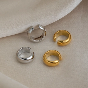 Dettaglio di ear cuff a C in oro e argento su un morbido tessuto di seta lucido