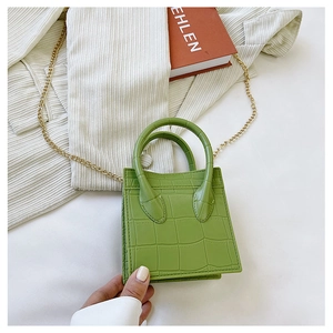 Detail of green crocodile embossed square bag with golden chain strap on white background
