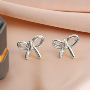 Close-up of silver bow stud earrings with a polished finish on pink silk background