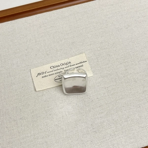 Detailed view of silver square metal ring with matte finish on textured grey cloth