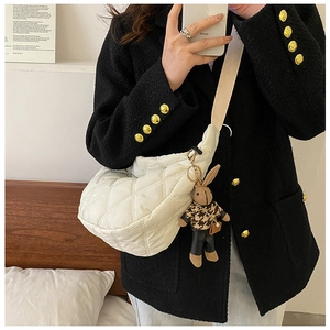 Detail of white quilted crescent bag featuring wide strap and brown plush rabbit charm