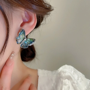 Model wearing a blue-green gradient butterfly earring with golden glitter and a pearl