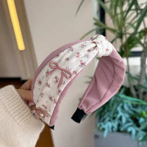 Floral embroidery headband with pink bow detail held against a natural green background