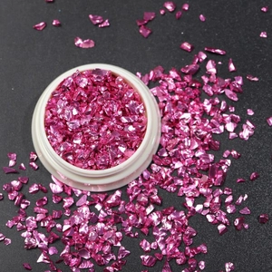 Macro shot of irregular pink iridescent nail art glass shards in a small white jar