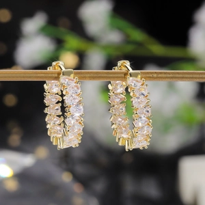 Macro detail of gold hoop earrings with tear-drop zircon stones on a decorative background