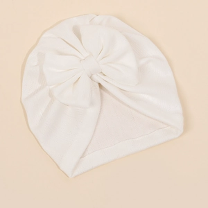 Détail d'un turban pour bébé blanc avec texture côtelée et un grand nœud en tricot