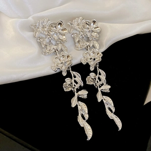Close-up of silver metal flower and leaf long tassel earrings on white silk fabric