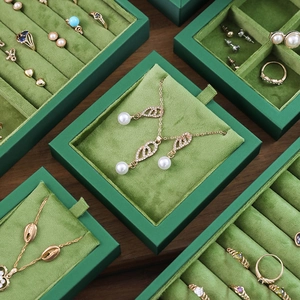 Green velvet jewelry organizers for rings and necklaces displayed on a wooden surface