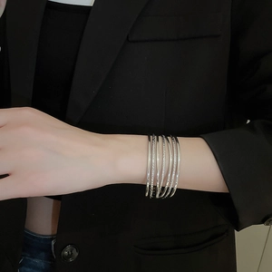 Detail of layered silver multi-strand cuff bracelet worn over a black blazer sleeve