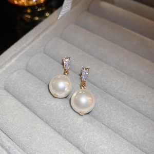 Macro view of gold-plated pearl drop earrings with triangular cubic zirconia detail
