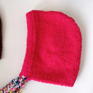 Macro detail of rose red plush knitted earflap hat with colorful mixed tassel cord