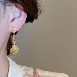 Close-up of gold hollow lantern drop earrings worn by a model in French court style