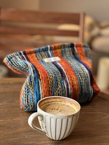 Detailaufnahme der farbenfrohen Boho-Stricktasche auf Holztisch mit Kaffeetasse