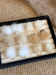 Macro shot of assorted plush fur ball earrings with pearls and metal rings on a tray