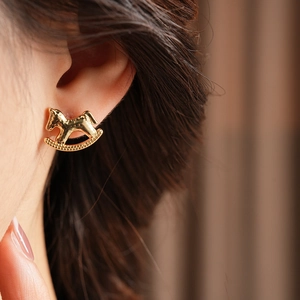 Close-up of golden rocking horse stud earrings with fine metal texture on model