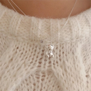Detail of silver double-layered necklace featuring a cute bear and zircon on a knit sweater