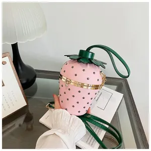Gros plan du sac seau fraise rose avec feuilles en cuir et bandoulière en chaîne