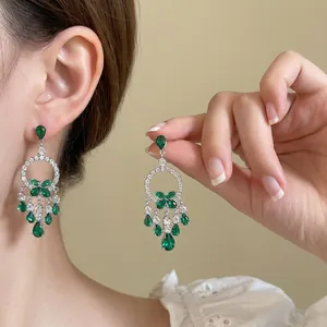 Détail de boucles d'oreilles argentées vintage avec pierres vert émeraude et nœuds en cristal