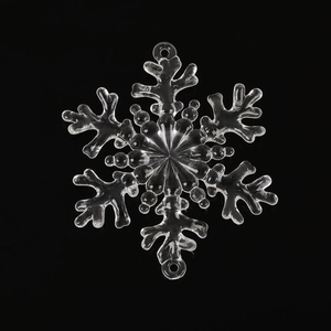 Macro shot of a transparent acrylic snowflake ornament with a top hanging loop on black backdrop
