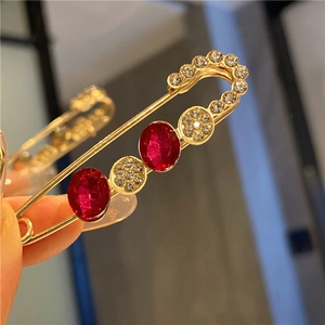 Detail of a gold-plated safety pin brooch featuring red oval gems and white rhinestones