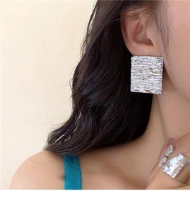 Detail of silver square stud earrings featuring unique brushed metal bark texture