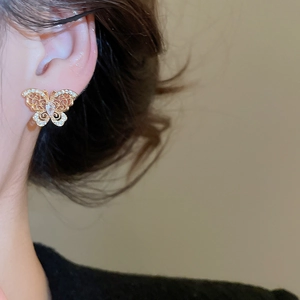 Detail of elegant gold butterfly stud earring with sparkling zircon on a model's ear