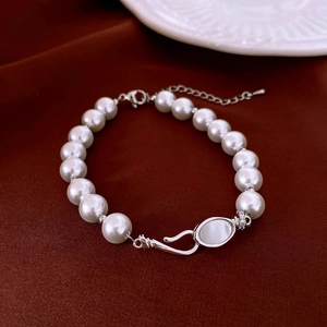 Detail of elegant pearl bracelet with silver clasp on a dark red silk background