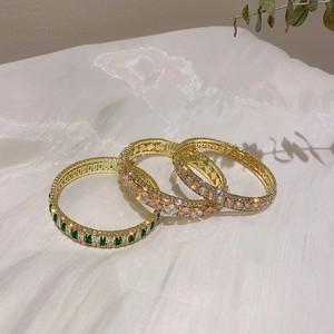 Detailed view of three gold-tone bangles with colorful gemstones on white satin fabric