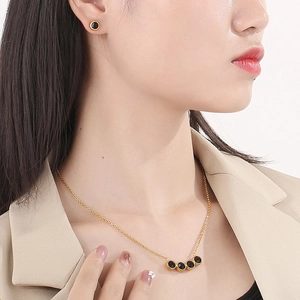 Dettaglio di parure in titanio dorato con collana e orecchini in zircone nero tondo
