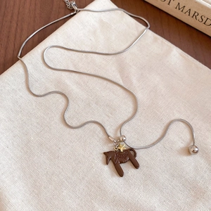 Detail of silver snake chain with brown horse pendant and gold star on linen